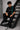 Man wearing a black Aston Martin oversized t-shirt with green racing stripes and the iconic Aston Martin wings logo, sitting on industrial stairs.