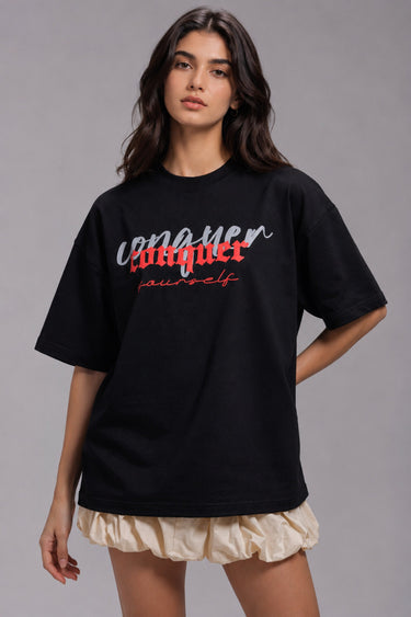 Black POPCASE oversized unisex tshirt with Conquer Yourself in layered red gothic and grey shadow text on front, styled with beige bubble shorts