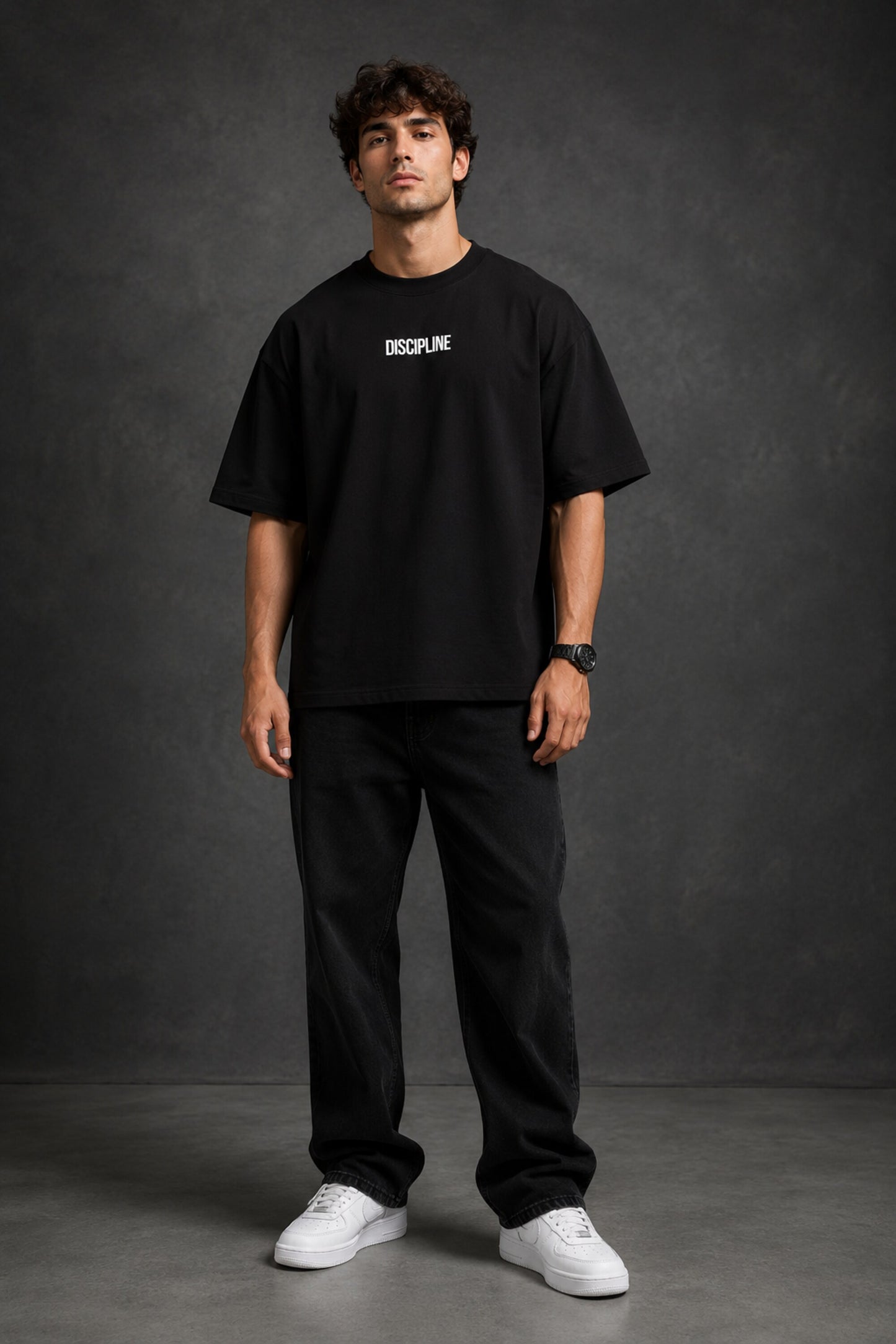 Man wearing a black DISCIPLINE WILD WOLF oversized t-shirt with white 'DISCIPLINE' text, dark wash jeans, and white sneakers, sitting on stairs. - black