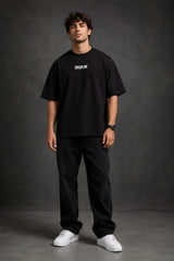 Man wearing a black DISCIPLINE WILD WOLF oversized t-shirt with white 'DISCIPLINE' text, dark wash jeans, and white sneakers, sitting on stairs. - black