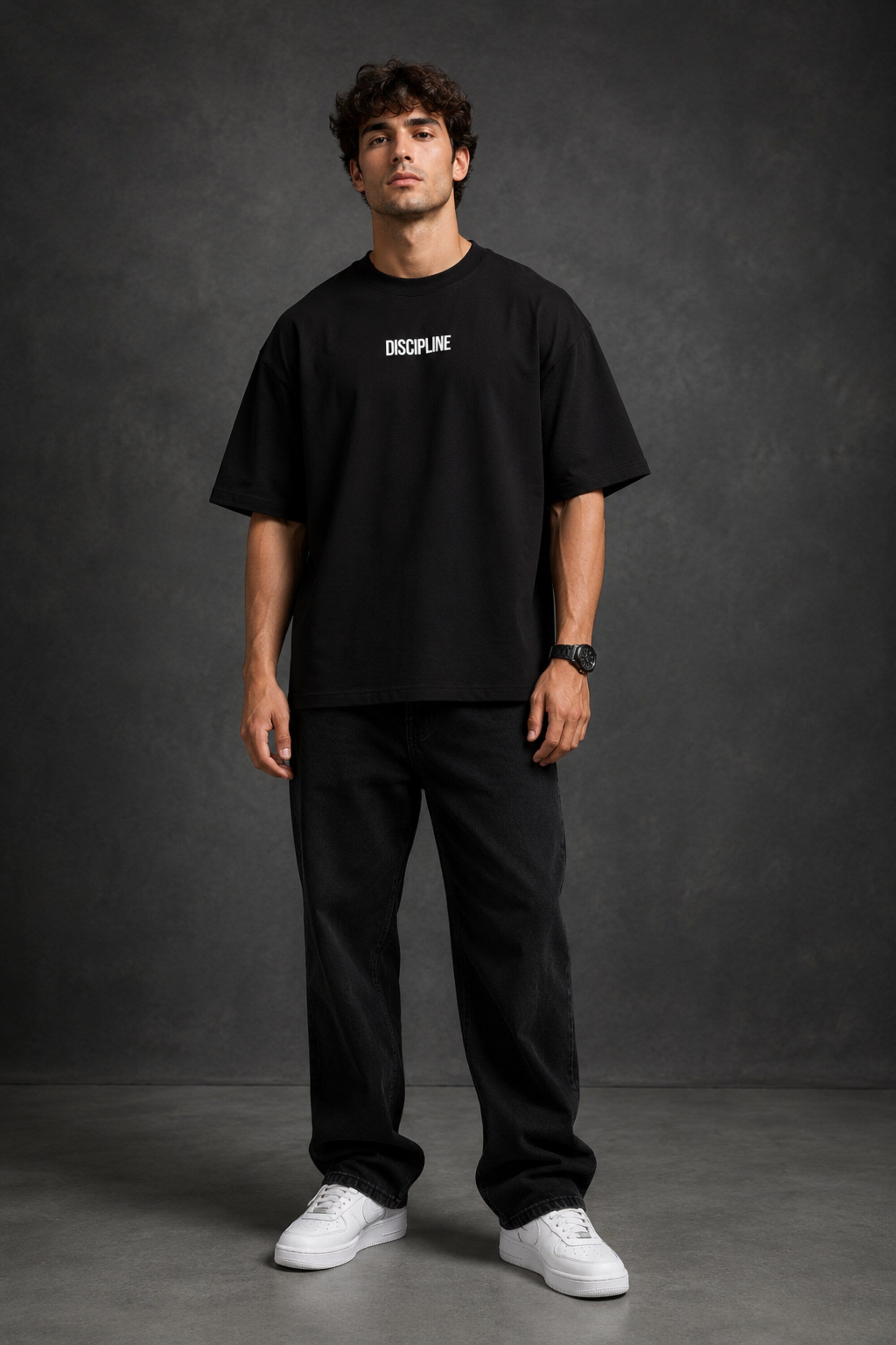 Man wearing a black DISCIPLINE WILD WOLF oversized t-shirt with white 'DISCIPLINE' text, dark wash jeans, and white sneakers, sitting on stairs. - black