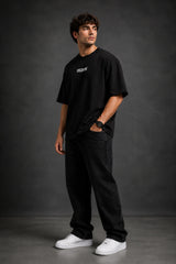 Man wearing a black DISCIPLINE WILD WOLF oversized t-shirt with white 'DISCIPLINE' text, dark wash jeans, and white sneakers, sitting on stairs.