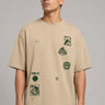 Back view of a man wearing a beige RARE INSIGHT oversized t-shirt with a green "Sorry But I Don't Care" graphic and star accents. - beige