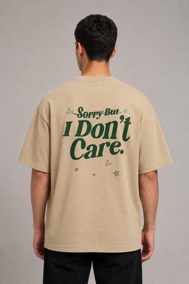 Back view of a man wearing a beige RARE INSIGHT oversized t-shirt with a green "Sorry But I Don't Care" graphic and star accents.