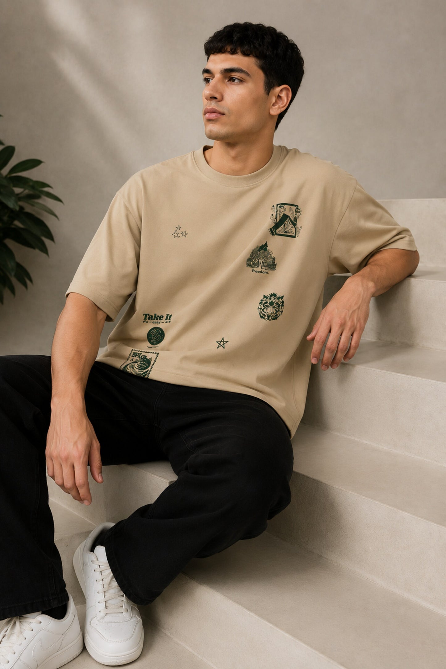 Back view of a man wearing a beige RARE INSIGHT oversized t-shirt with a green "Sorry But I Don't Care" graphic and star accents.