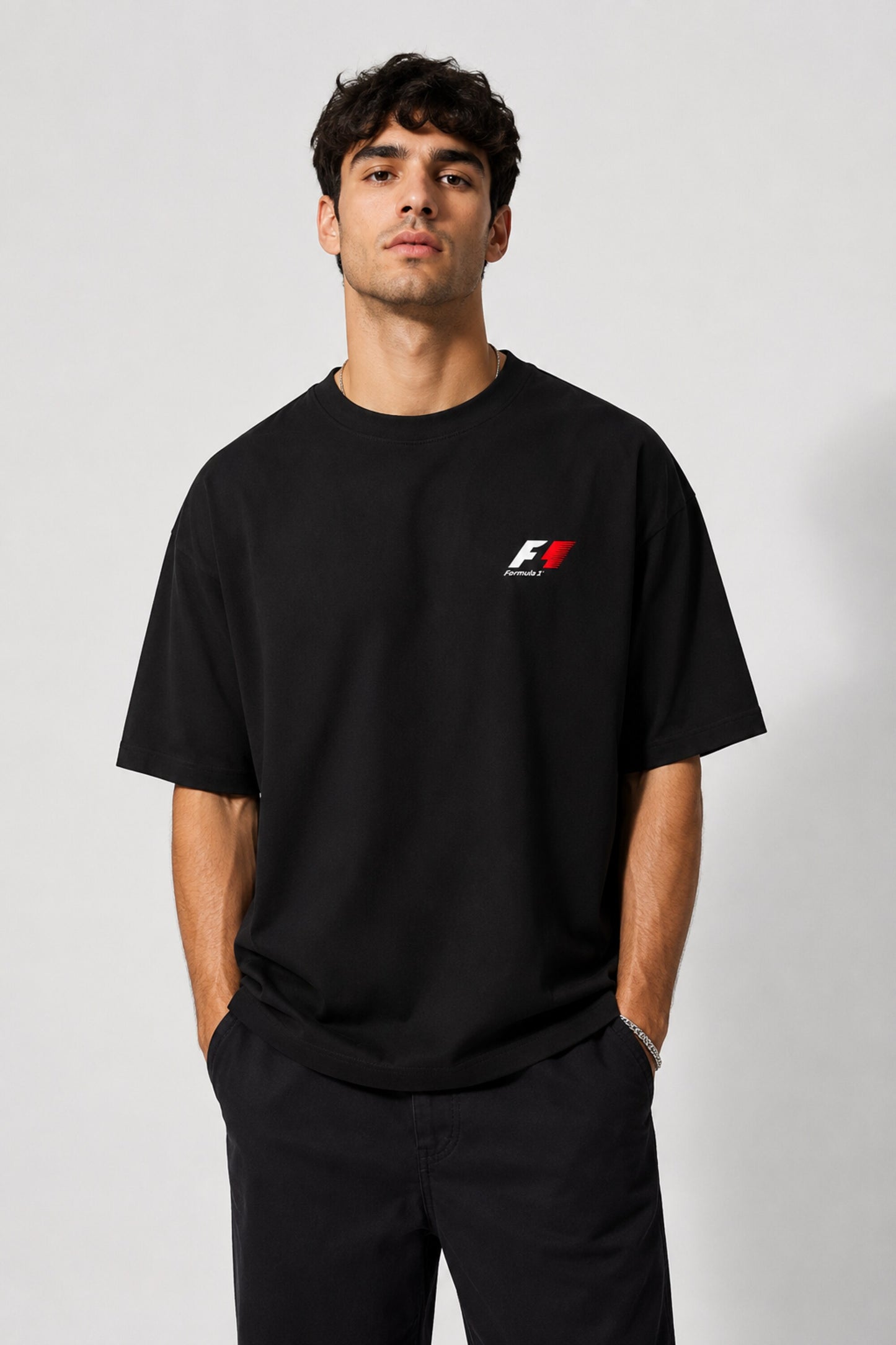 Model wearing a black oversized t-shirt with a small, embroidered Formula 1® logo in white, red, and gray on the chest. Casual streetwear style.
