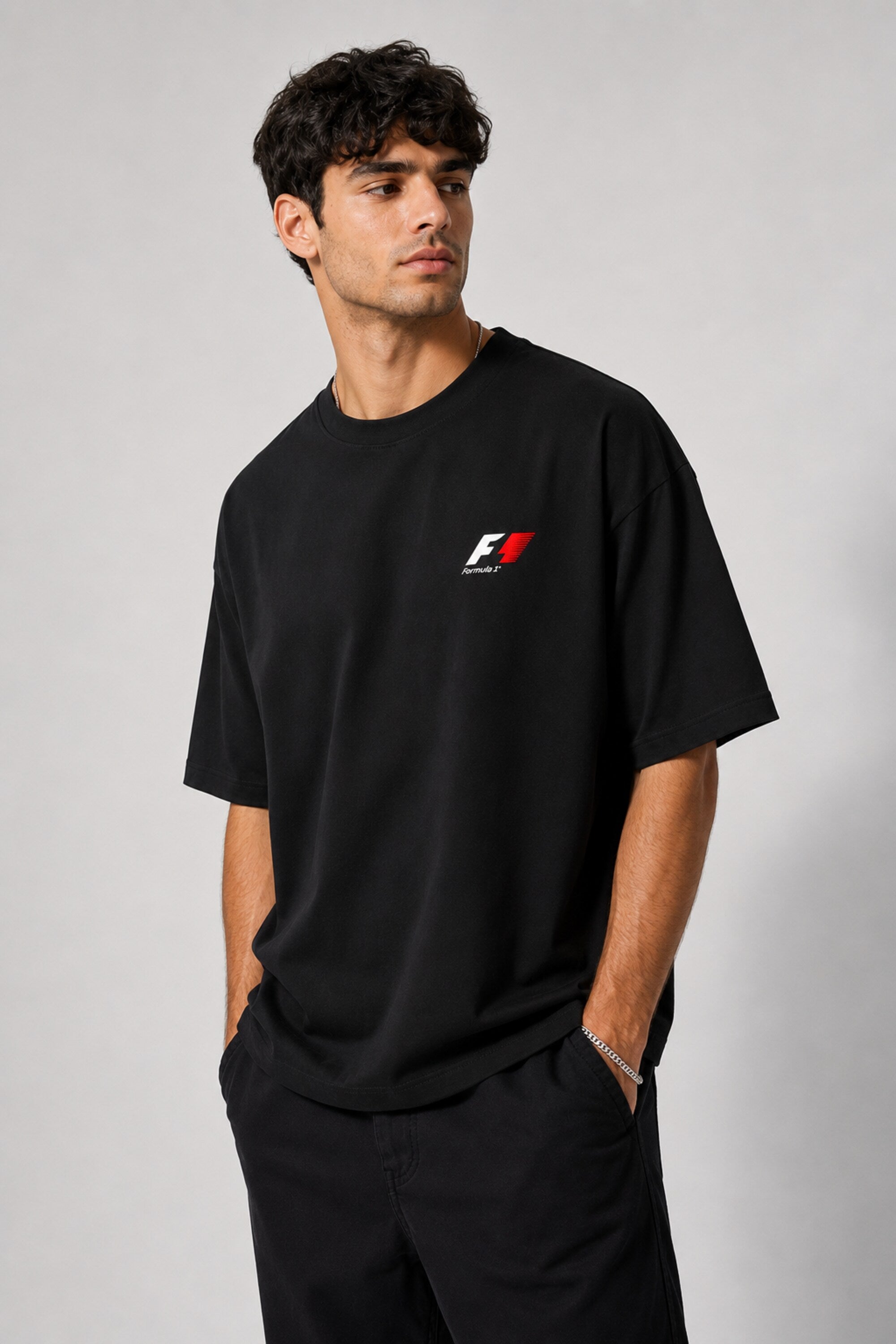 Model wearing a black oversized t-shirt with a small, embroidered Formula 1® logo in white, red, and gray on the chest. Casual streetwear style.