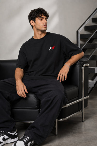 Model wearing a black oversized t-shirt with a small, embroidered Formula 1® logo in white, red, and gray on the chest. Casual streetwear style.