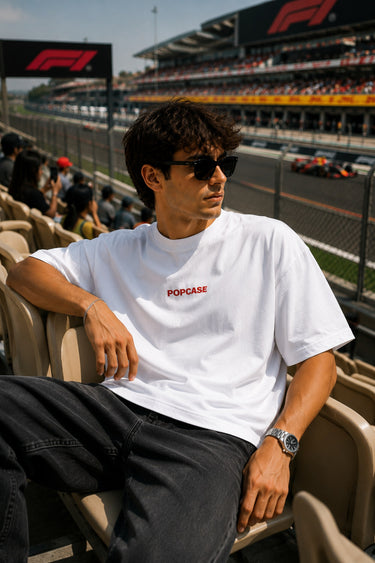 Man wearing sunglasses and a white t-shirt with 'POPCASE' logo at a Formula 1 event.