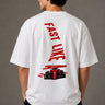 Man wearing white F1 Official oversized t-shirt with red F1 logo, black wide-leg jeans, and white sneakers, sitting on a black leather couch. - white