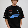 Model wearing a black Fast Feels Forever oversized t-shirt with graphic prints, sitting on a leather couch. - black