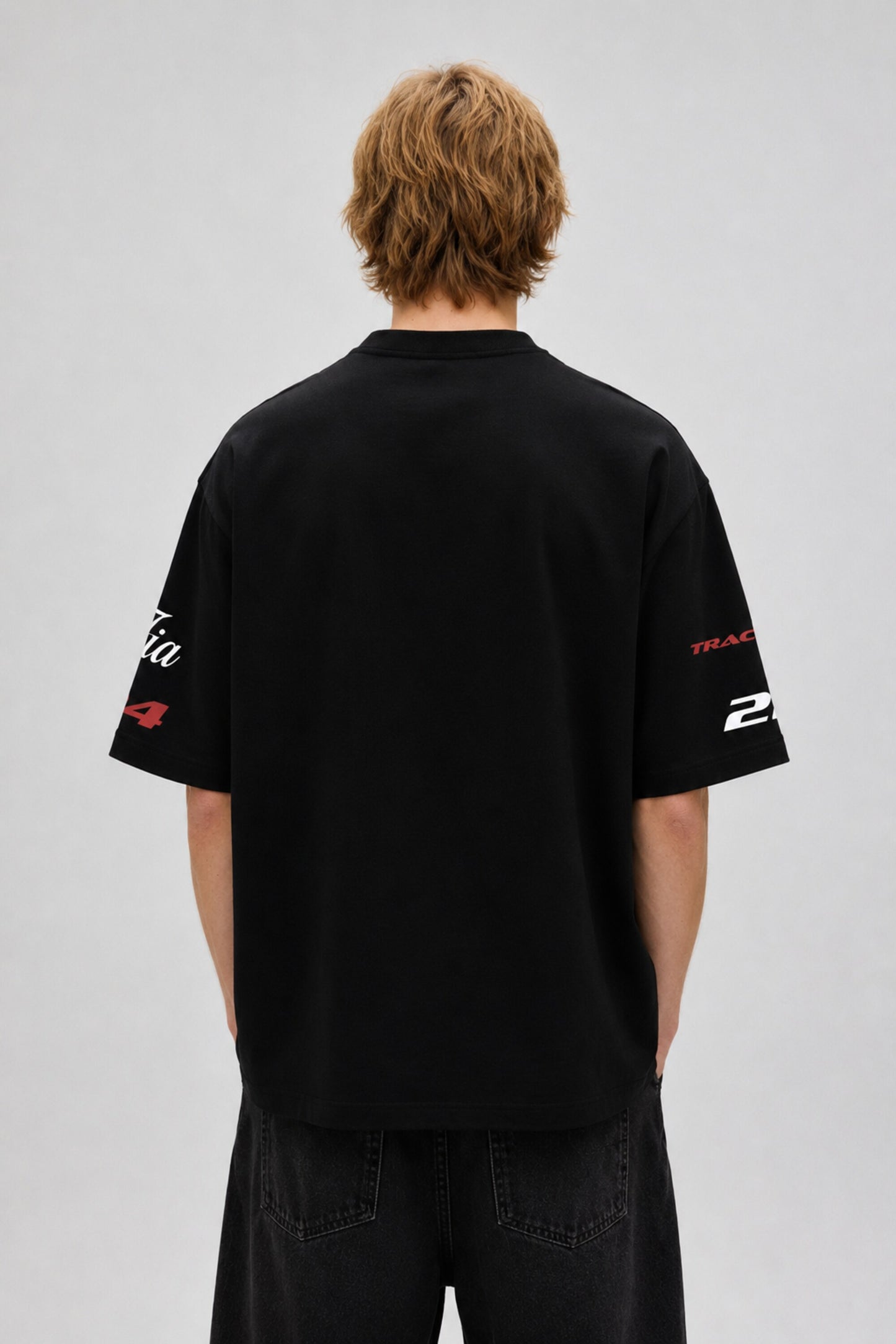 Model wearing a black Fast Feels Forever oversized t-shirt with graphic prints, sitting on a leather couch.