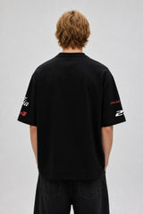Model wearing a black Fast Feels Forever oversized t-shirt with graphic prints, sitting on a leather couch.