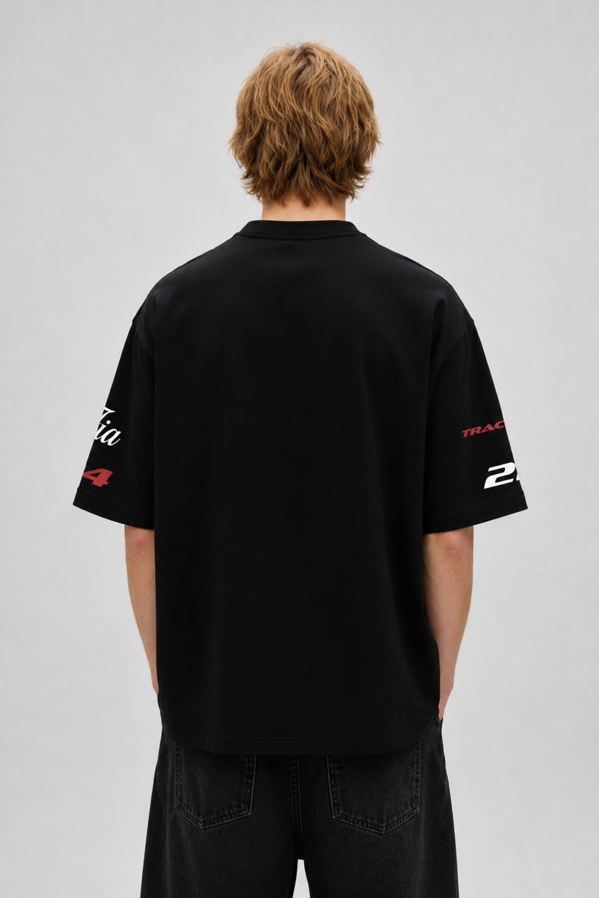 Model wearing a black Fast Feels Forever oversized t-shirt with graphic prints, sitting on a leather couch.