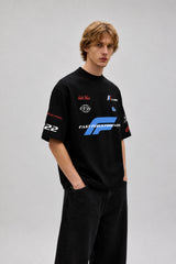 Model wearing a black Fast Feels Forever oversized t-shirt with graphic prints, sitting on a leather couch.