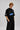 Model wearing a black Fast Feels Forever oversized t-shirt with graphic prints, sitting on a leather couch.