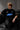 Model wearing a black Fast Feels Forever oversized t-shirt with graphic prints, sitting on a leather couch.