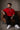 Man wearing a red FCB Messi fan oversized t-shirt, black pants, and white sneakers, sitting on a brown couch.