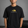 Man wearing FROM THE NORTH oversized t-shirt in beige with black cargo pants and white sneakers. Features The North Face logo and graphic on front and back.