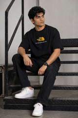 Man wearing FROM THE NORTH oversized t-shirt in beige with black cargo pants and white sneakers. Features The North Face logo and graphic on front and back.