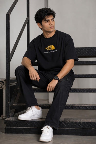 Man wearing FROM THE NORTH oversized t-shirt in beige with black cargo pants and white sneakers. Features The North Face logo and graphic on front and back.