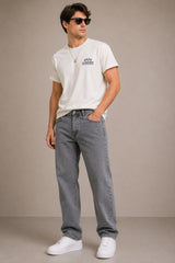 Man wearing a white t-shirt with a logo and gray jeans against a beige background