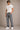 Man wearing a white t-shirt with a logo and gray jeans against a beige background
