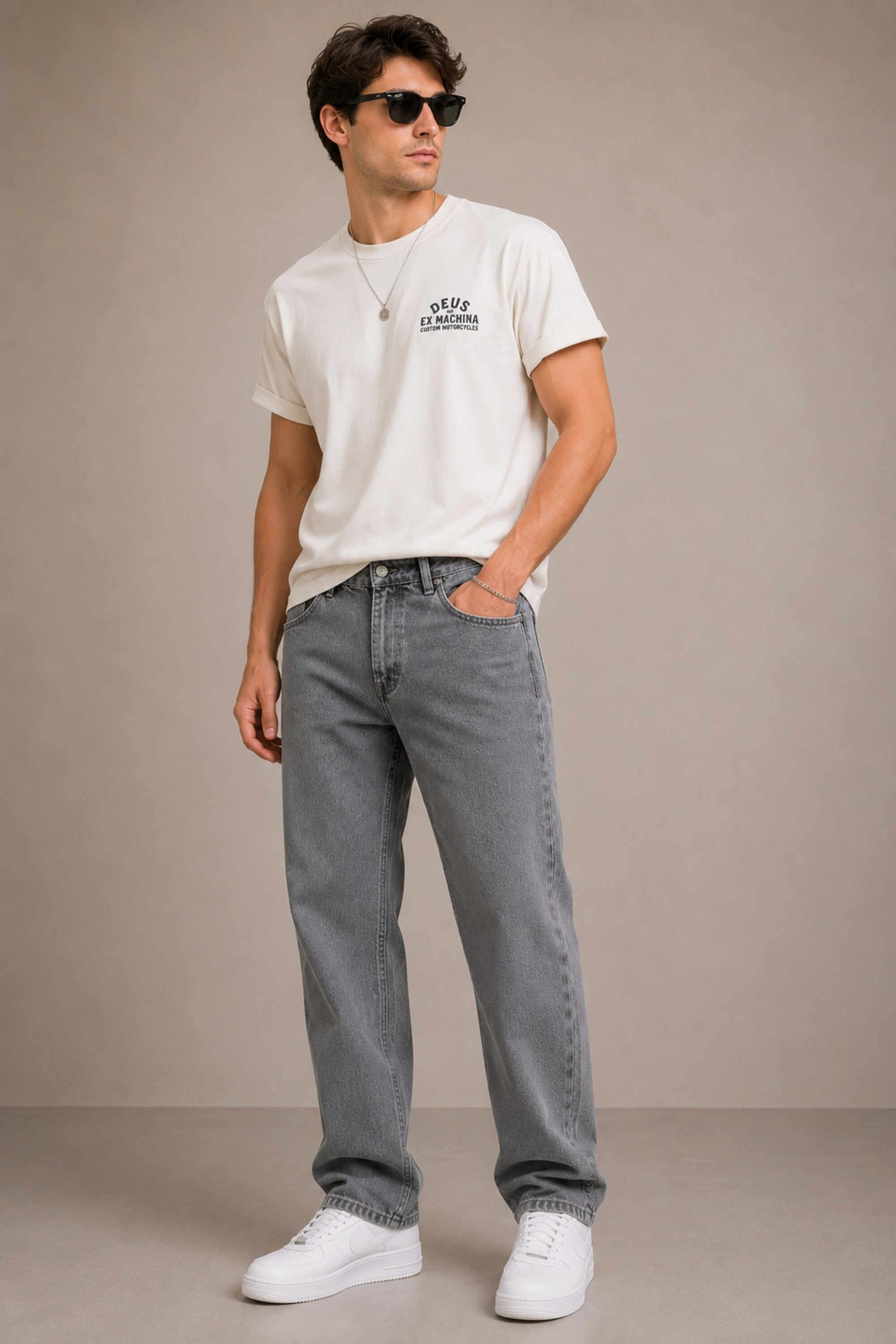Man wearing a white t-shirt with a logo and gray jeans against a beige background