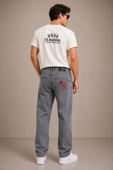 Man wearing a white t-shirt with 'Deus Ex Machina' logo and gray jeans on a beige background