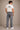 Man wearing a white t-shirt with 'Deus Ex Machina' logo and gray jeans on a beige background