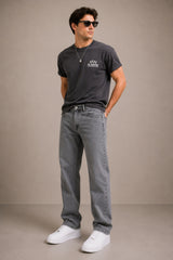 Man wearing a dark gray t-shirt, jeans, and white sneakers against a beige background