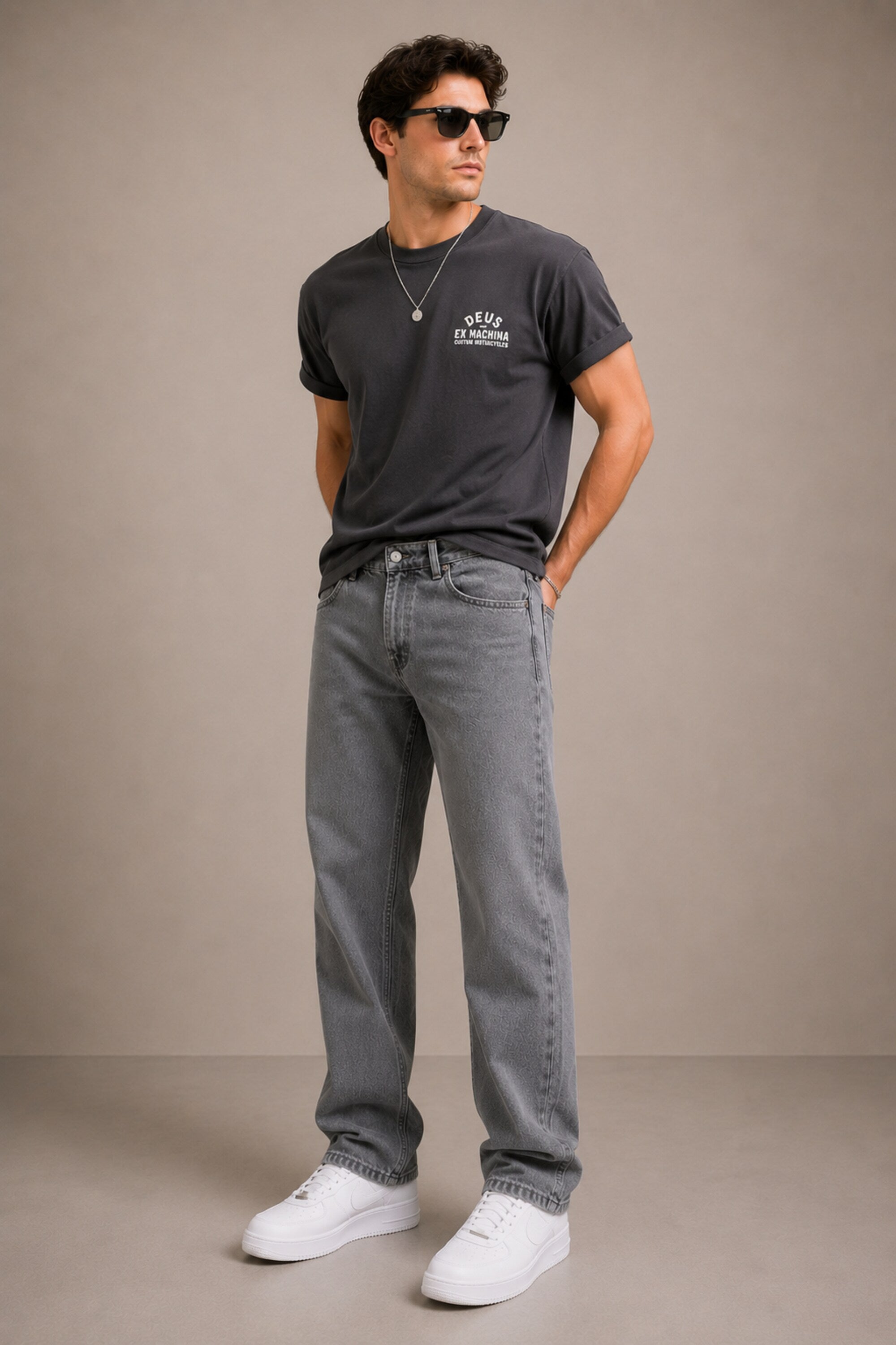 Man wearing a dark gray t-shirt, jeans, and white sneakers against a beige background