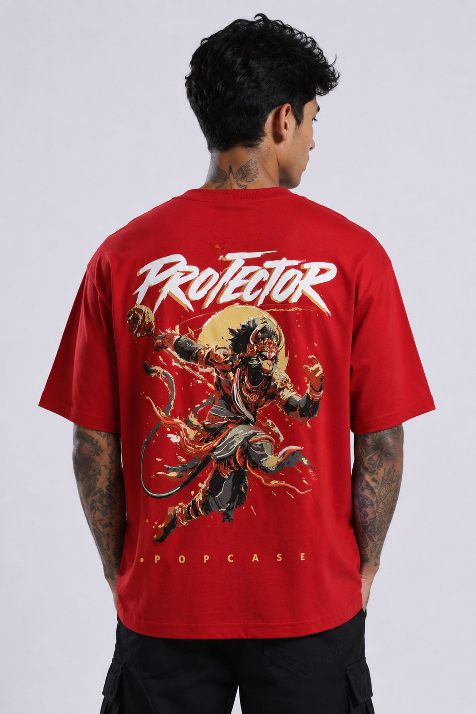 Red oversized t-shirt with 'PROJECTOR HANUMANJI' graphic design of a warrior monkey god and 'POPCASE' logo, worn by a man.