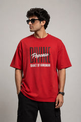 Man wearing a red PROJECTOR HANUMANJI oversized t-shirt with black pants and white sneakers, sitting on metal stairs.
