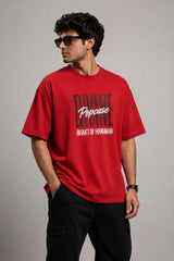 Man wearing a red PROJECTOR HANUMANJI oversized t-shirt with black pants and white sneakers, sitting on metal stairs.