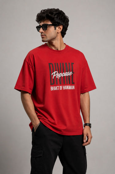 Man wearing a red PROJECTOR HANUMANJI oversized t-shirt with black pants and white sneakers, sitting on metal stairs.