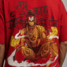 Man wearing a red PROJECTOR HANUMANJI oversized t-shirt with black pants and white sneakers, sitting on metal stairs. - red