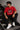 Man wearing a red PROJECTOR HANUMANJI oversized t-shirt with black pants and white sneakers, sitting on metal stairs.