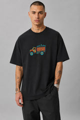 Back view of a man wearing a black HORN OK PLEASE oversized t-shirt with gold 'POPCASE' logo on the upper back.