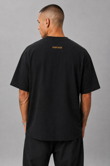 Back view of a man wearing a black HORN OK PLEASE oversized t-shirt with gold 'POPCASE' logo on the upper back.