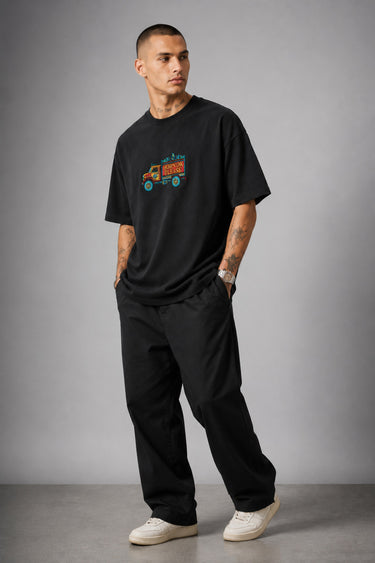 Back view of a man wearing a black HORN OK PLEASE oversized t-shirt with gold 'POPCASE' logo on the upper back.