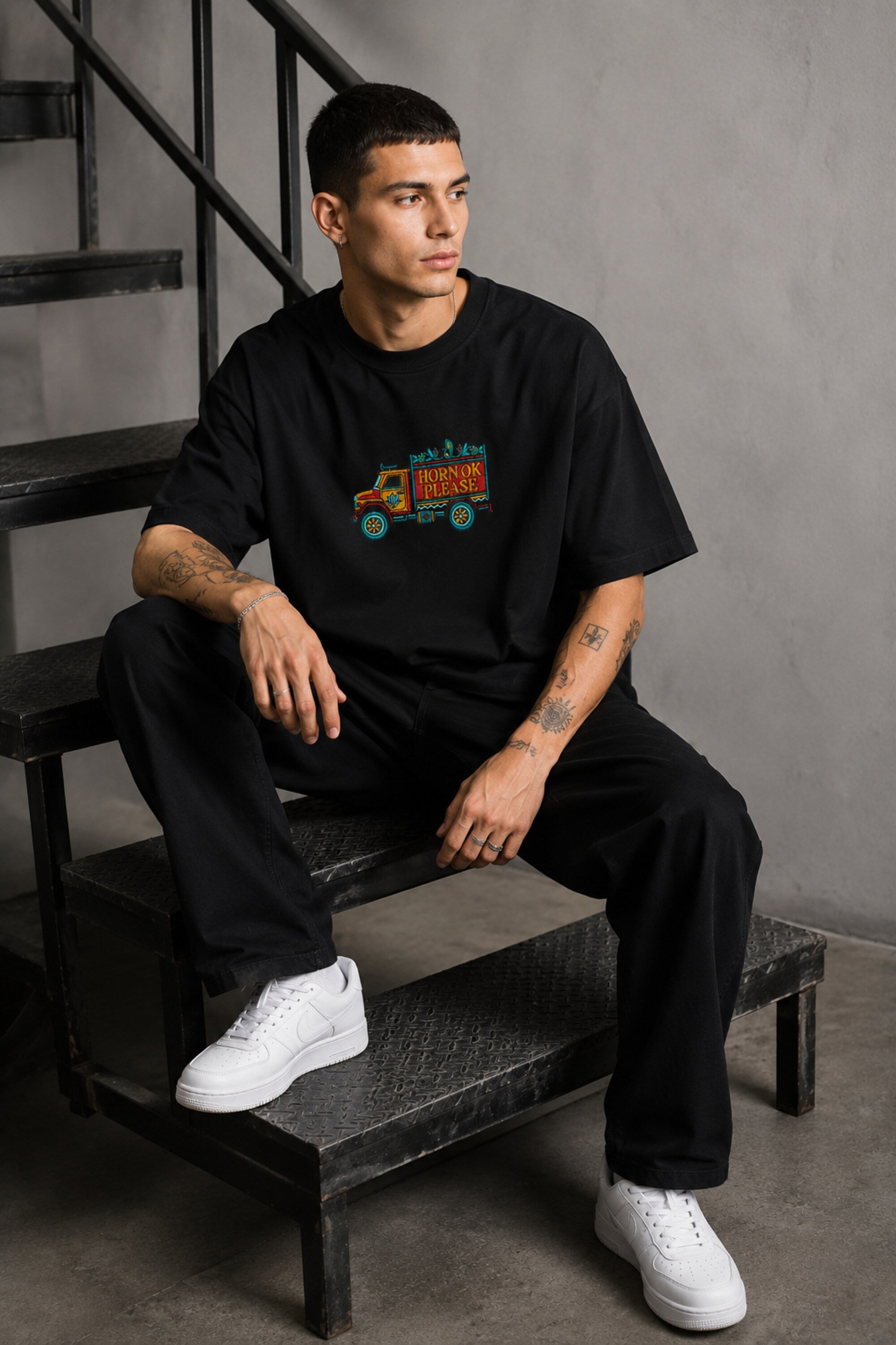 Back view of a man wearing a black HORN OK PLEASE oversized t-shirt with gold 'POPCASE' logo on the upper back.