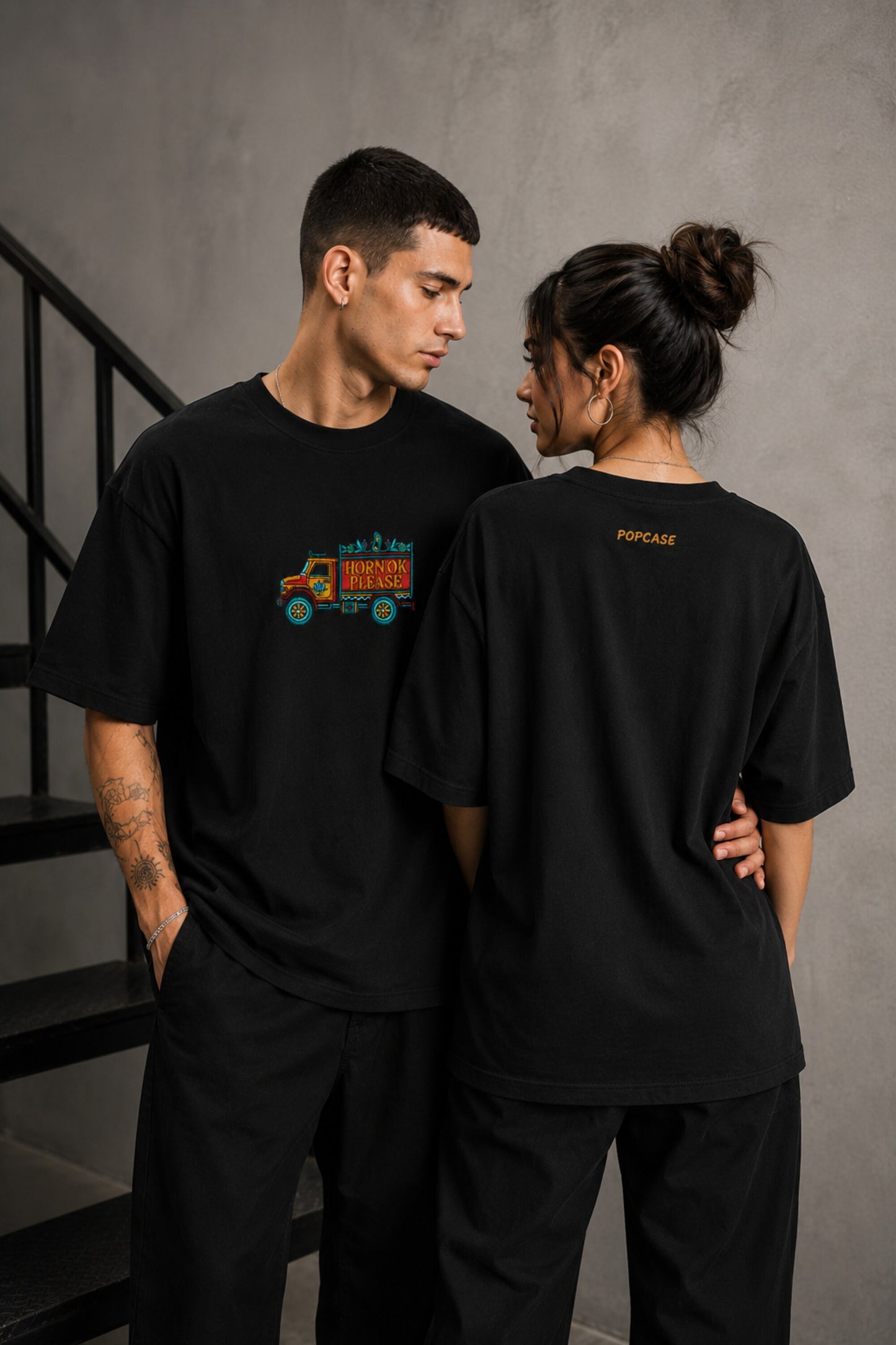 Back view of a man wearing a black HORN OK PLEASE oversized t-shirt with gold 'POPCASE' logo on the upper back.