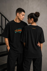 Back view of a man wearing a black HORN OK PLEASE oversized t-shirt with gold 'POPCASE' logo on the upper back.