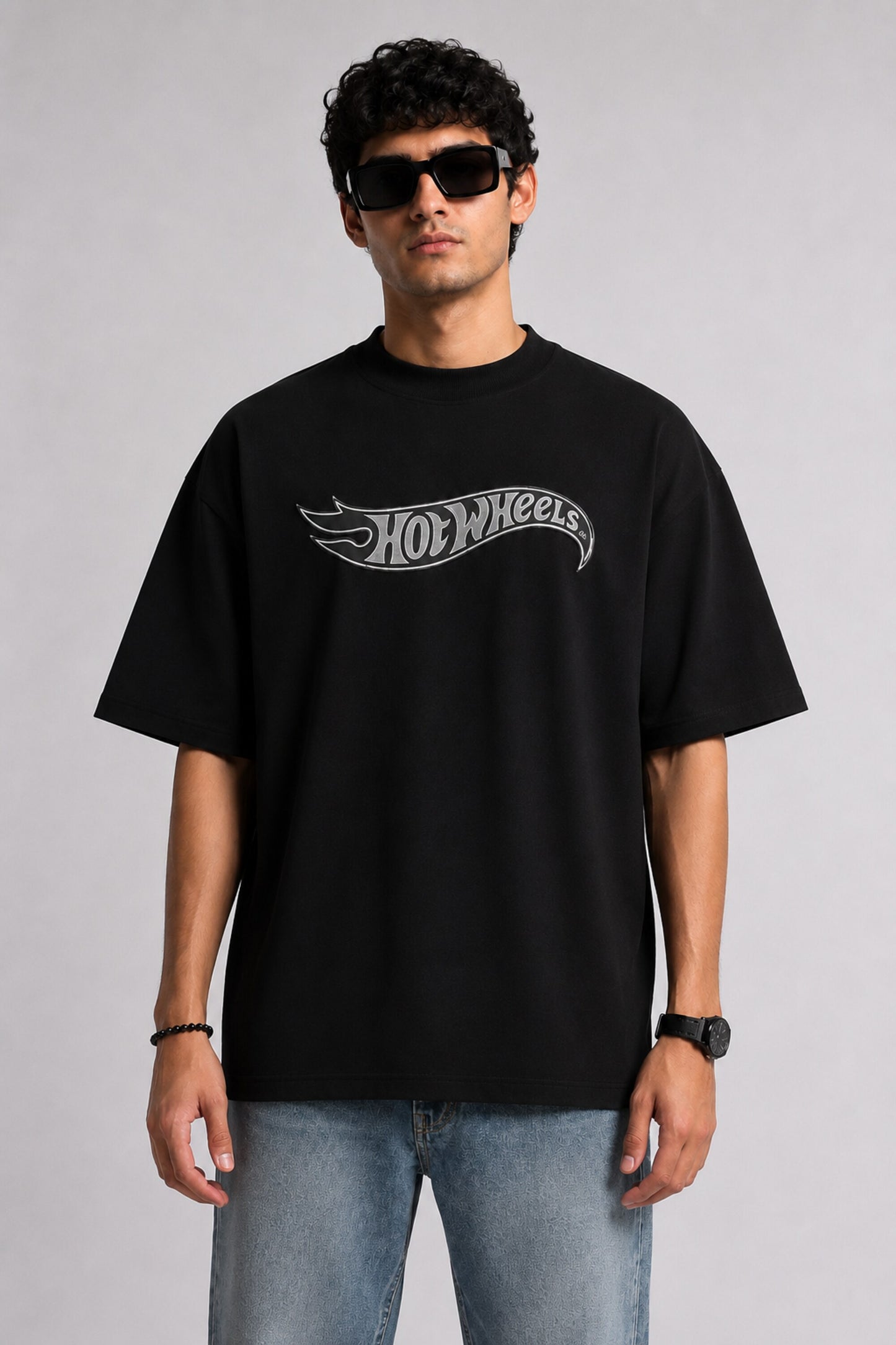 A couple wearing matching black oversized Hot Wheels t-shirts and light wash jeans, posing intimately against a neutral background.
