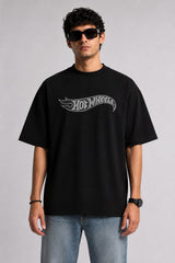 A couple wearing matching black oversized Hot Wheels t-shirts and light wash jeans, posing intimately against a neutral background.