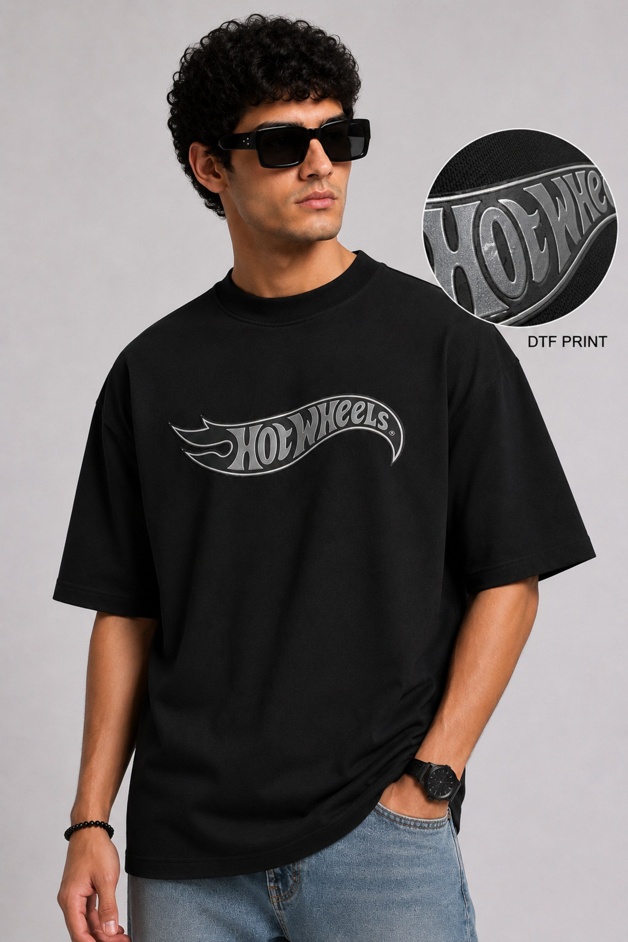 A couple wearing matching black oversized Hot Wheels t-shirts and light wash jeans, posing intimately against a neutral background.