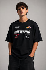 Man wearing a black STAR BOY oversized t-shirt with "Hot Wheels" graphics, sitting on a black couch. Streetwear fashion. - black