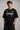Man wearing a black STAR BOY oversized t-shirt with "Hot Wheels" graphics, sitting on a black couch. Streetwear fashion. - black