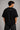Man wearing a black STAR BOY oversized t-shirt with "Hot Wheels" graphics, sitting on a black couch. Streetwear fashion.